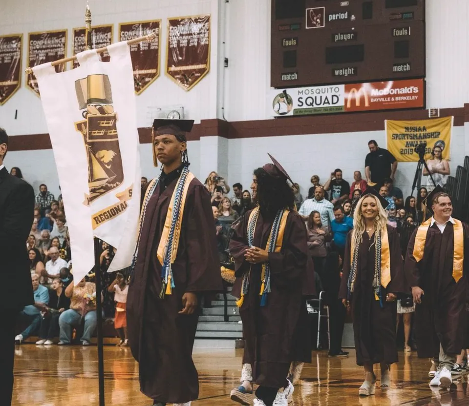 Studenti della Central Regional High School in toga da diploma stanno davanti a un McDonald's con striscioni.