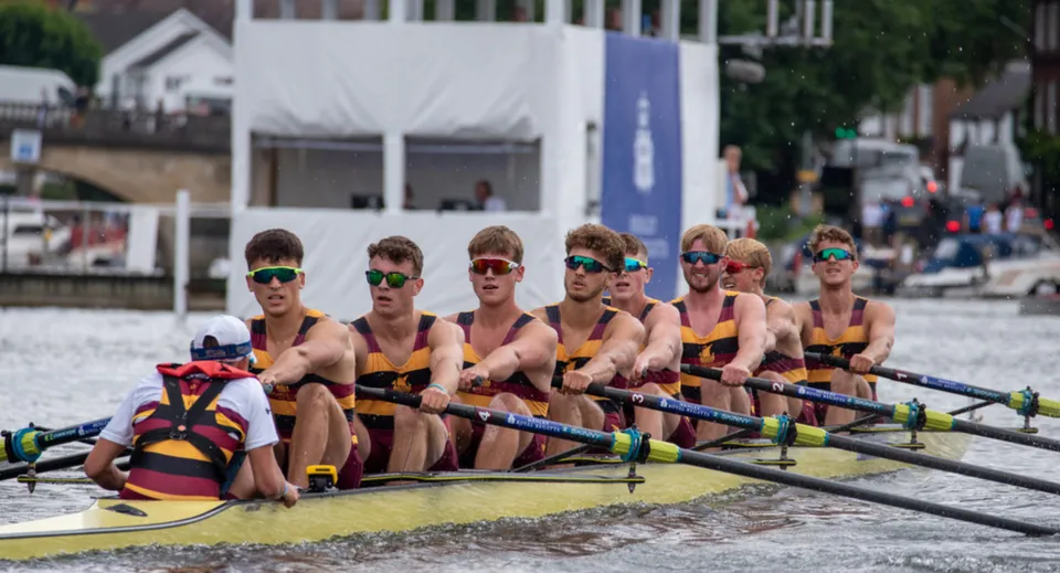 Un gruppo di canottieri in divise colorate è seduto su una barca in acqua nell'area del Shiplake College.