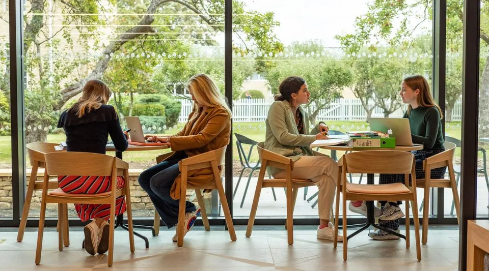 Un gruppo di studentesse della St. Mary’s Calne siede in un accogliente caffè con un'ampia vista sul verde attraverso le finestre.