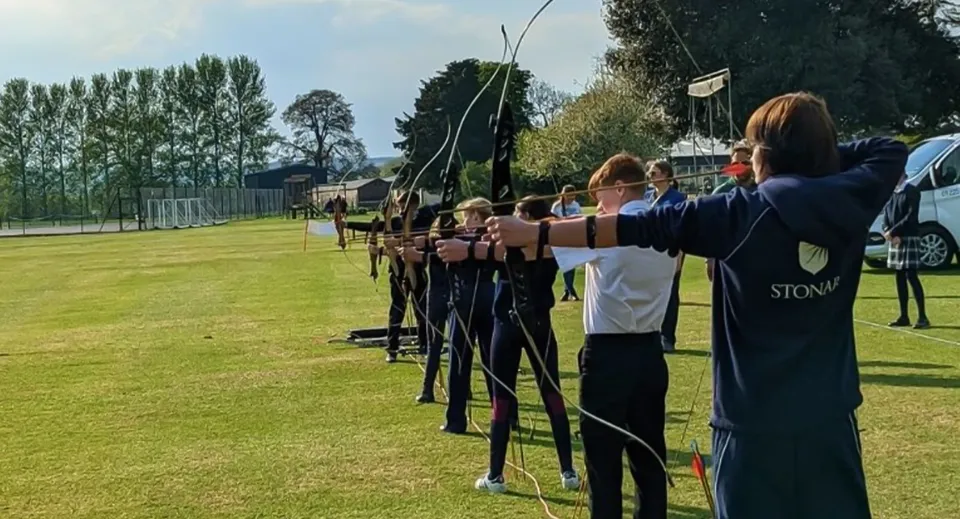 Studenti della Stonar School si trovano in un campo e tirano con l'arco verso i bersagli.