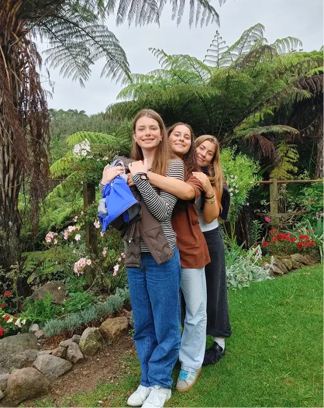 Tre studentesse si abbracciano in un giardino rigoglioso con felci arboree e fiori in Nuova Zelanda