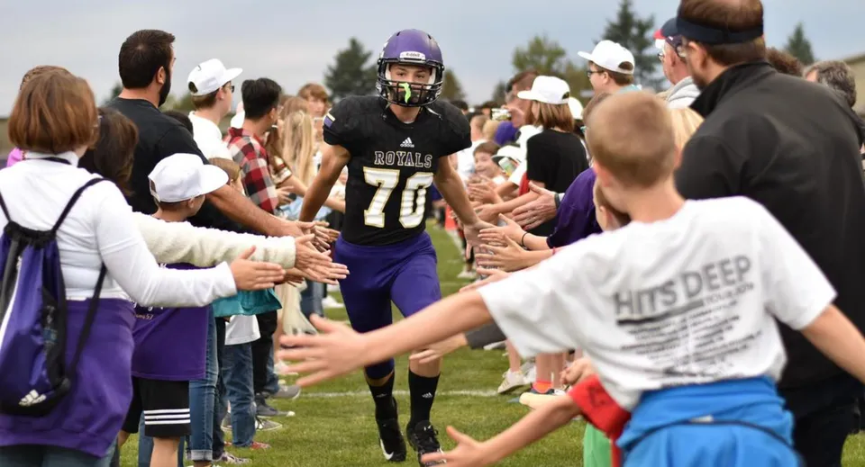 Studenti della Portland Christian High School si radunano in divisa sportiva su un campo da gioco mentre gli spettatori assistono sullo sfondo.