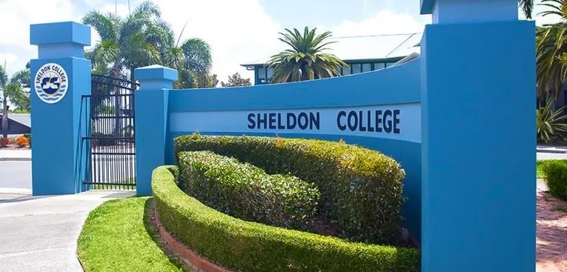 L'ingresso del Sheldon College con cancello blu e cartello circondato da palme e siepi curate.