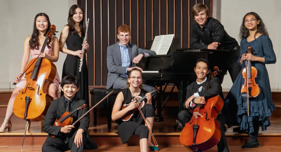 Un gruppo di musicisti della St. Peter’s High School suona diversi strumenti su un palco con sfondo in legno.