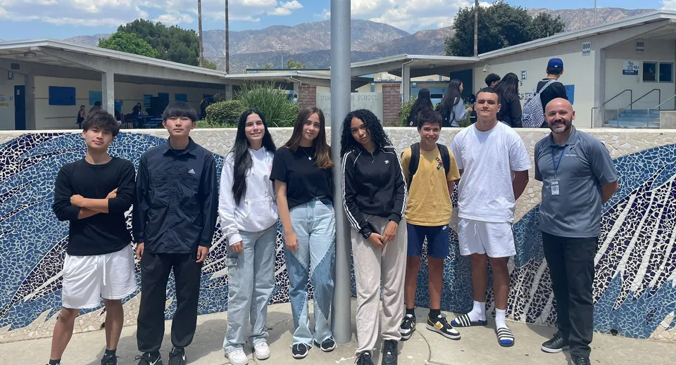 Un gruppo di studenti e studentesse si trova davanti a un edificio con le montagne sullo sfondo nella sede del Duarte Unified School District.