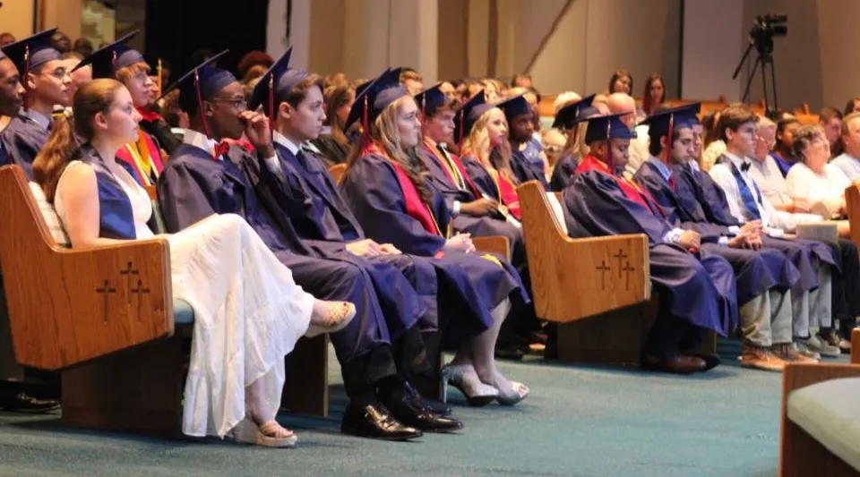 Neodiplomati della Faith Christian School siedono in toga a una cerimonia di diploma con palco e pubblico.