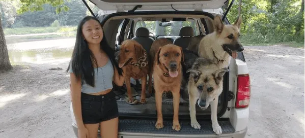 Chica sonriente de pie junto al maletero abierto de un coche lleno de perros