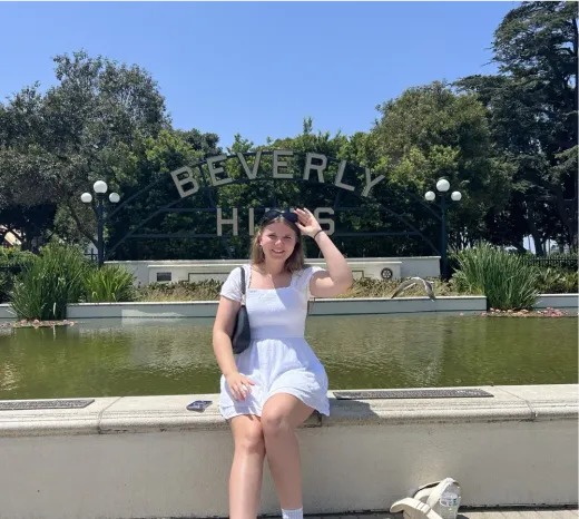 Ragazza in abito bianco posa davanti all'insegna di Beverly Hills negli Stati Uniti.