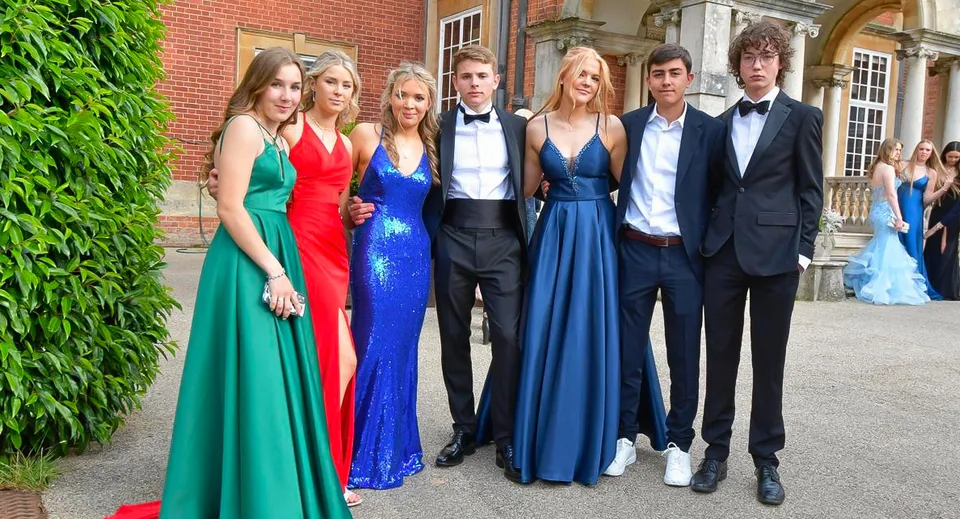 Un gruppo di studenti della Sherfield School vestiti in modo elegante si trova davanti a un edificio in mattoni circondato dal verde.
