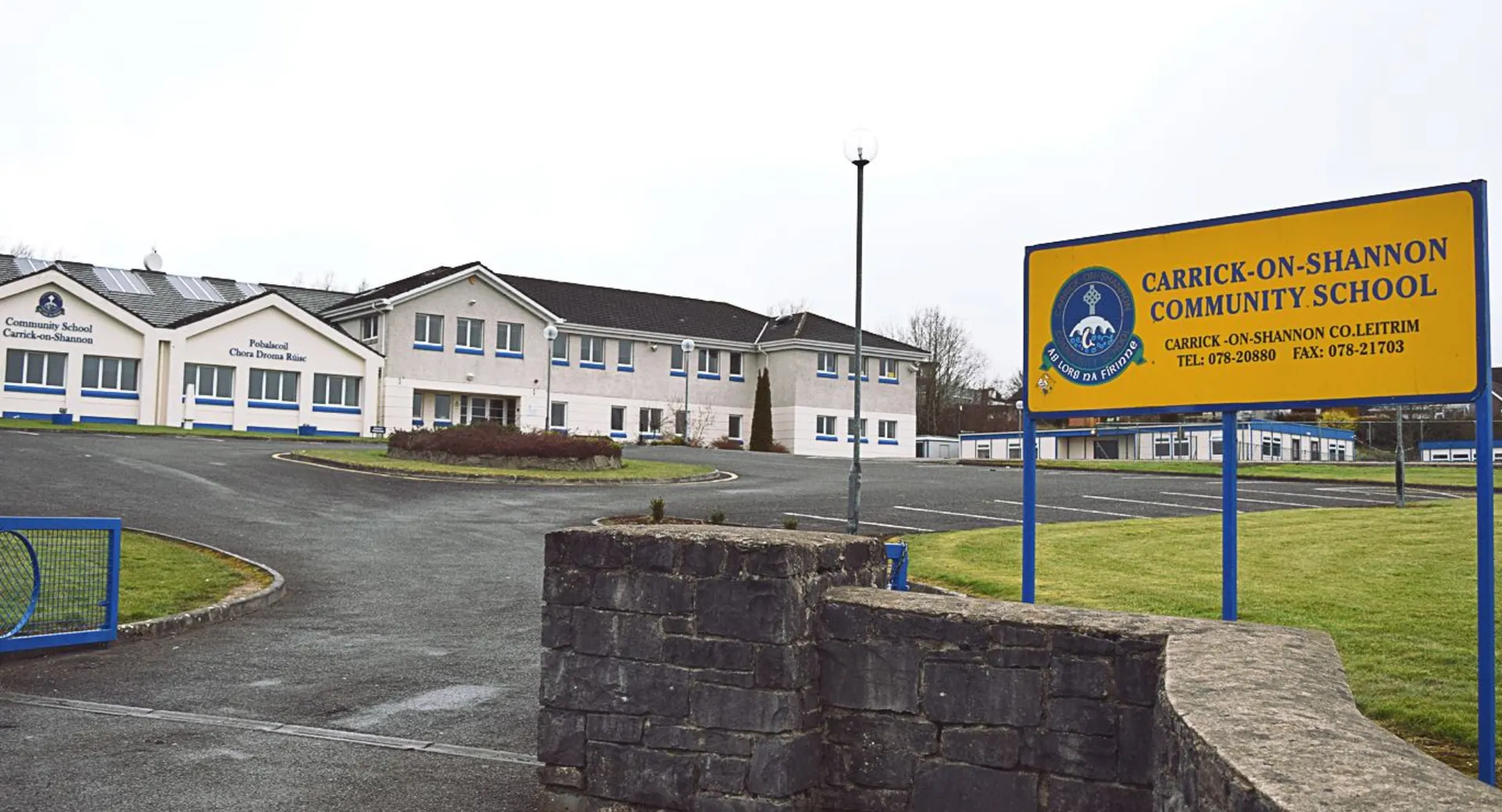 L'edificio della Carrick on Shannon Community School con un muro di pietra in primo piano, circondato da un'area pavimentata e altri edifici.