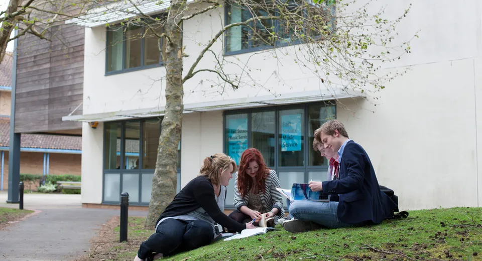 Un gruppo di studenti dell'East Sussex College Lewes è seduto sull'erba davanti a un edificio e chiacchiera.