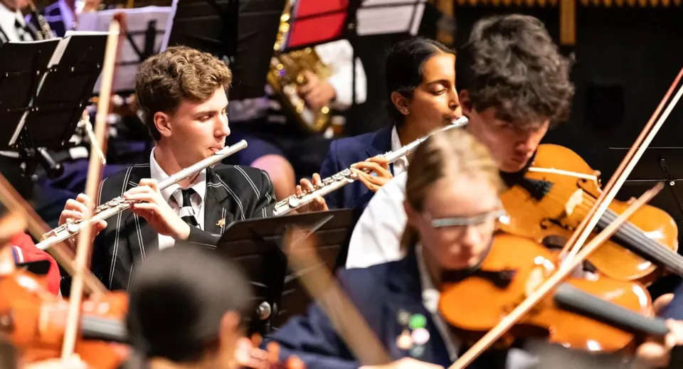 Un gruppo di studenti del Christ's College suona vari strumenti su un palco con uno sfondo colorato.