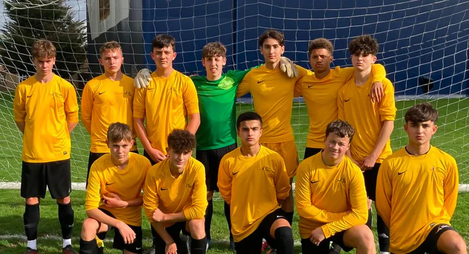 Un gruppo di giovani calciatori in maglia gialla posa davanti a una rete blu sul campo sportivo dell'Oak Leaf Studio.