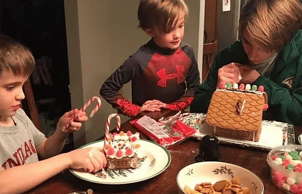 Tres niños decoran casitas de jengibre con golosinas alrededor de una mesa
