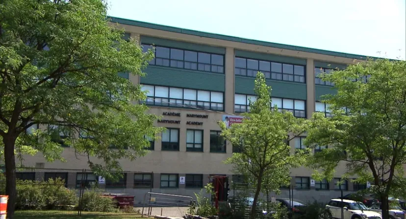 L'edificio a più piani dipinto di verde della Marymount Academy International è circondato da alberi verdi.