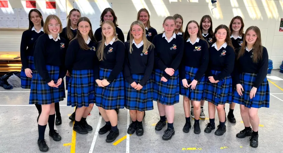 Un gruppo di studentesse della St. Raphaela’s Secondary School sta insieme davanti a un edificio con grandi finestre.