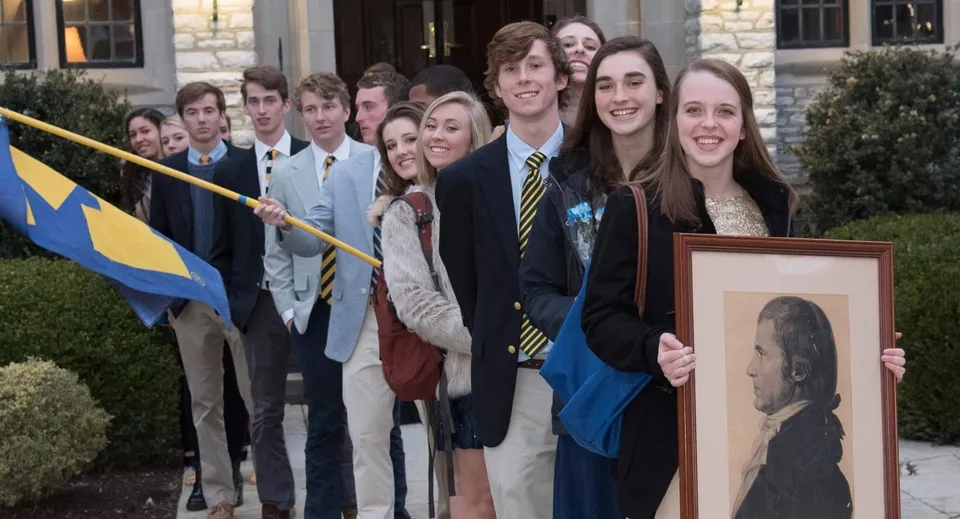 Un gruppo di studenti della Mercersburg Academy sta con un ritratto incorniciato davanti a un edificio con una bandiera.