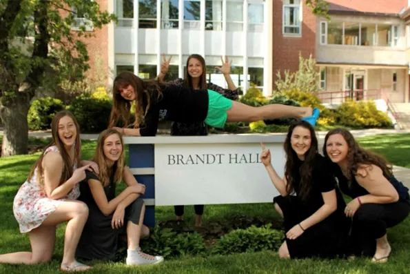 Varias jóvenes sonrientes posan divertidas junto a un cartel donde pone Brandt Hall