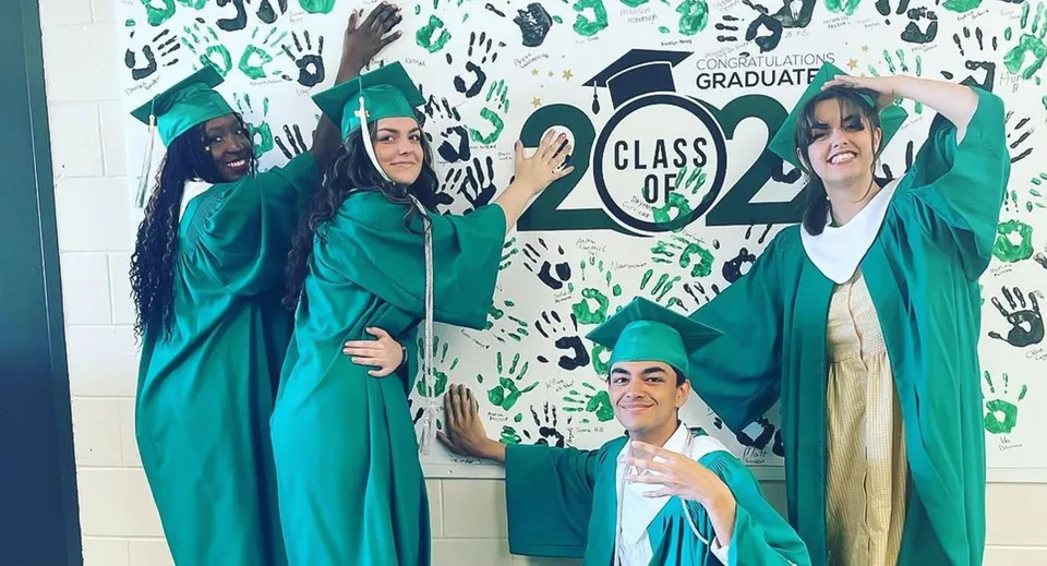 I diplomati e le diplomate del Murdoch Mackay Collegiate in toga verde posano davanti a uno sfondo con la scritta CLASS OF 2024 e impronte di mani.