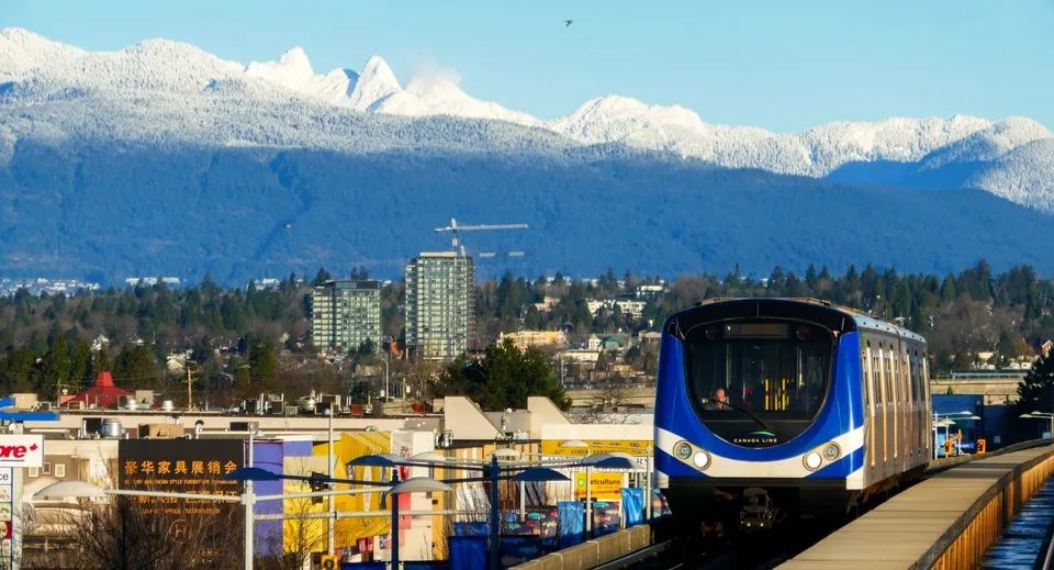 Un treno leggero moderno transita davanti a montagne innevate vicino alla Canada Star Secondary School.