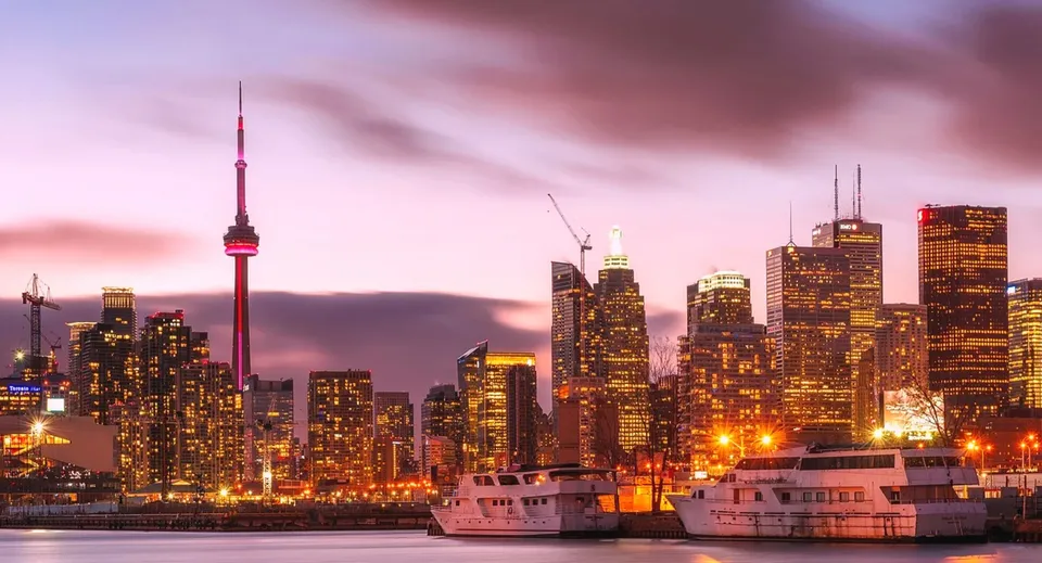 Lo skyline illuminato di Toronto con la CN Tower e imbarcazioni nel porto al tramonto.