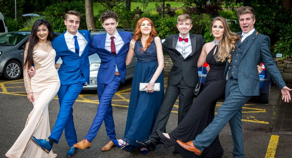 Un gruppo di persone eleganti nel campus della Lewes Old Grammar School davanti a uno sfondo verde.