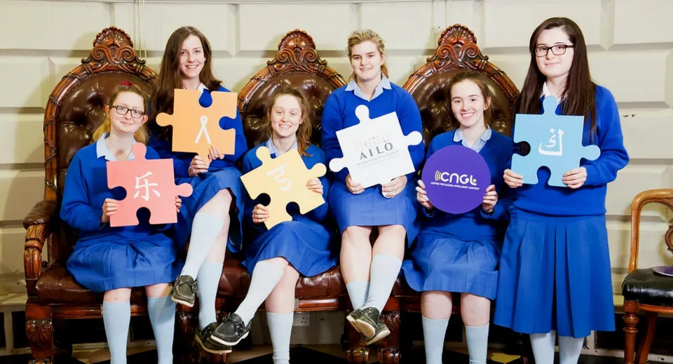 Un gruppo di giovani studentesse della St. Joseph of Cluny School si trova davanti a una parete di legno decorata tenendo in mano dei pezzi di puzzle.