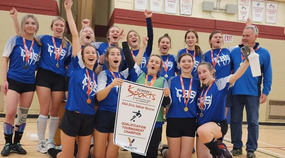 Studentesse della Clarenville High School festeggiano la loro vittoria con medaglie e coppa davanti a una parete dipinta di rosso.