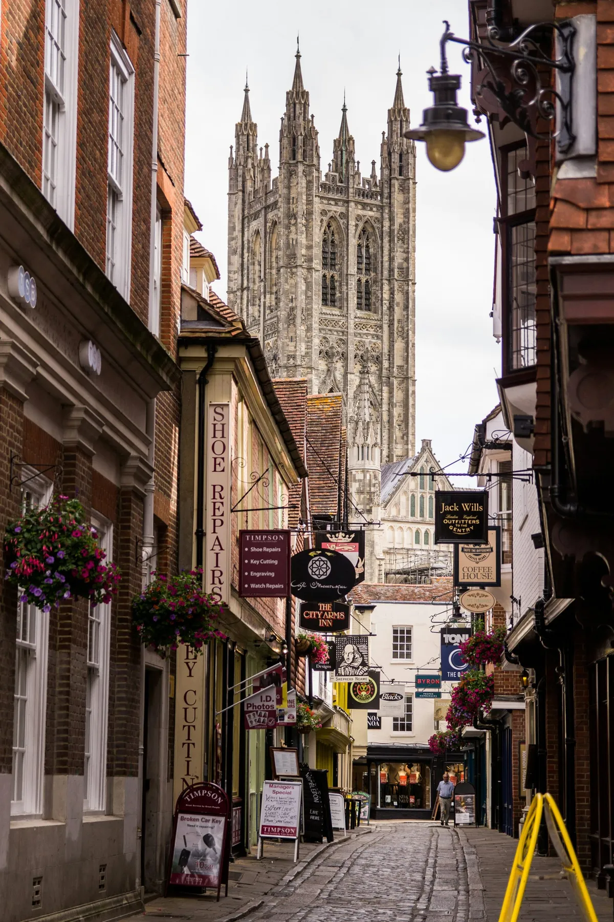 Vicolo pedonale di Canterbury con le insegne dei negozi e la torre della cattedrale sullo sfondo