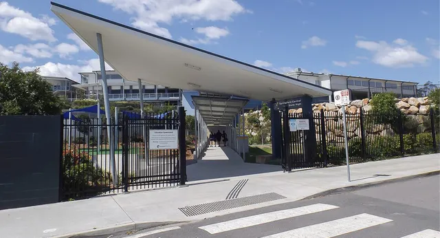 L'edificio principale moderno della Springfield Central State High School con tetto spiovente e un'area recintata è visibile in primo piano.