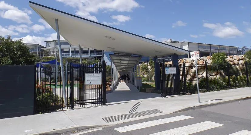 L'edificio principale moderno della Springfield Central State High School con tetto spiovente e un'area recintata è visibile in primo piano.