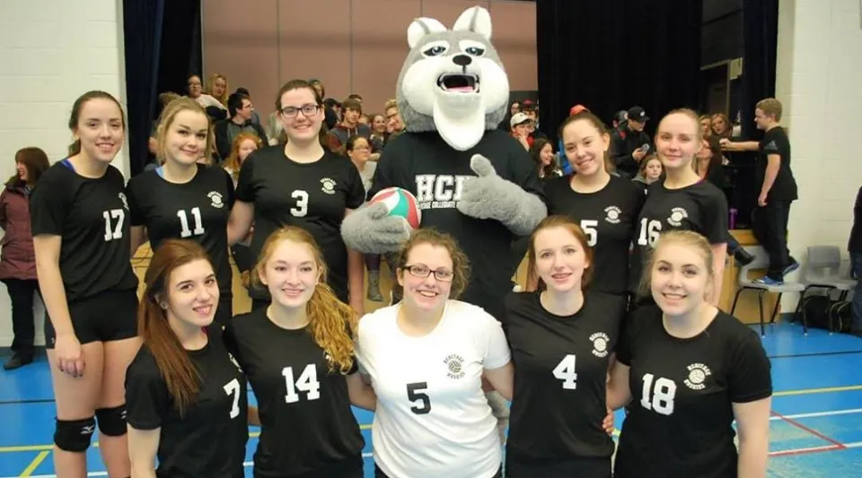 Un gruppo di giovani atlete della Leo Burke Academy posa insieme alla grande mascotte bianca nella palestra.