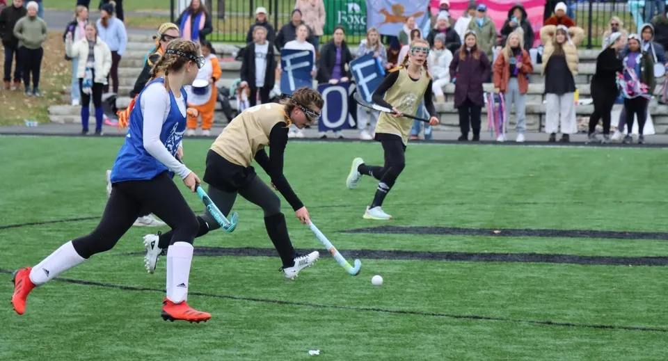 Studentesse della Foxcroft School giocano a hockey su prato su un campo sportivo davanti al pubblico.