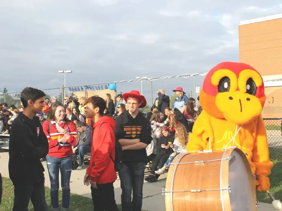 Un grande personaggio dei cartoni animati giallo si trova davanti a una folla nel campus della Resurrection Catholic School.