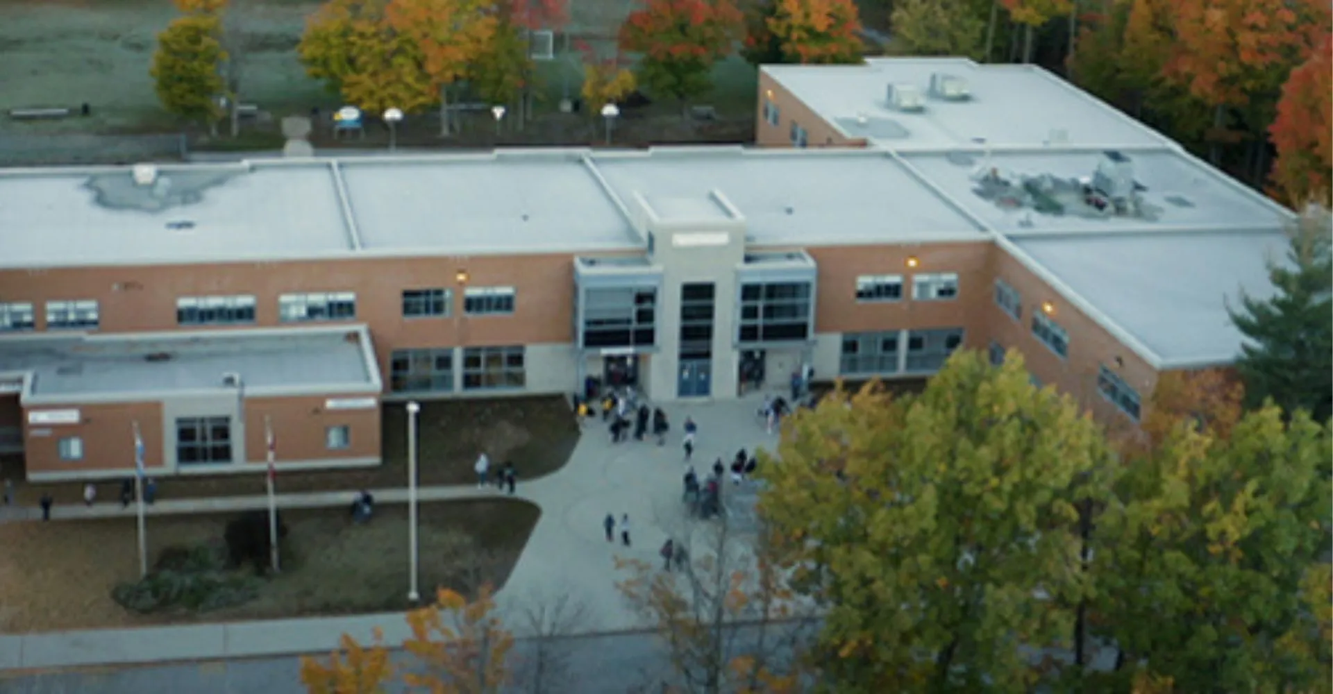 L'edificio a più piani con facciata in vetro del campus della Westwood High School è immerso in un contesto autunnale con alberi e persone.