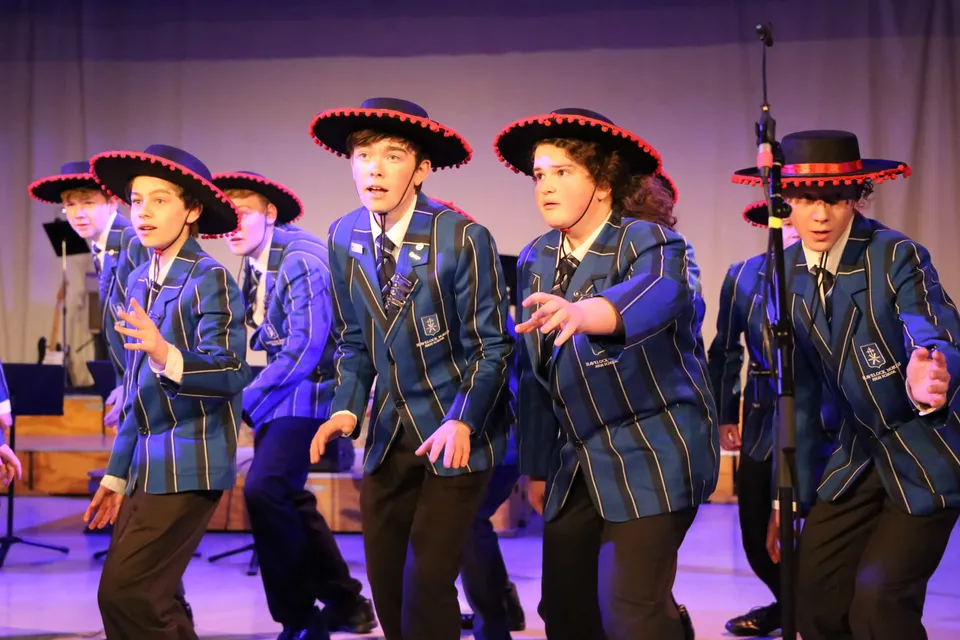 Studenti della Havelock North High School si esibiscono su un palco con sfondo viola indossando divise blu e cappelli rossi.