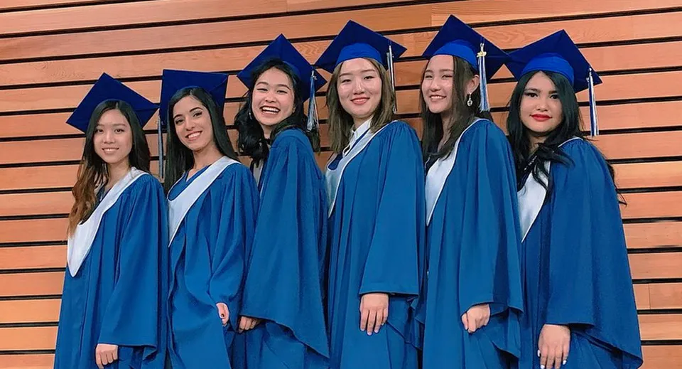 Un gruppo di studentesse in toga blu da diplomande festeggia il proprio diploma davanti a una parete di legno nel campus della Sentinel Secondary School.