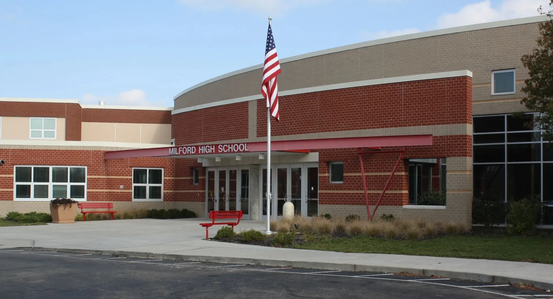 Il moderno edificio in mattoni e vetro del Milford Public School District è circondato da un parcheggio e da una bandiera americana sul tetto.