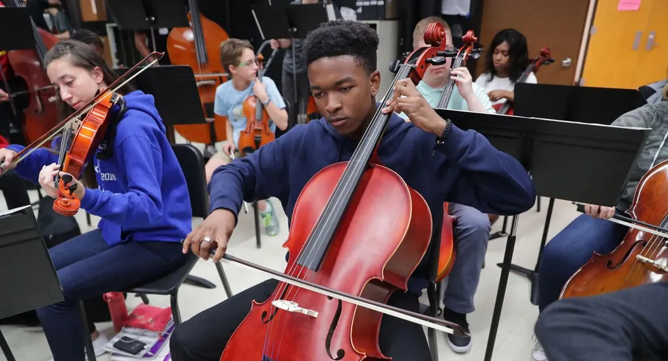 Uno studente delle Desert Sands Schools suona con concentrazione un grande violoncello rosso durante una prova musicale.