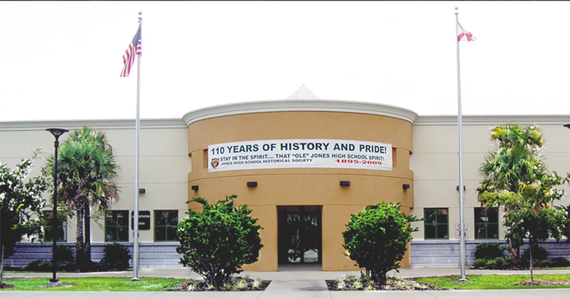 L'edificio della Jones High School con il grande cartello "110 years of history and pride" e bandiere visibili è circondato da palme.