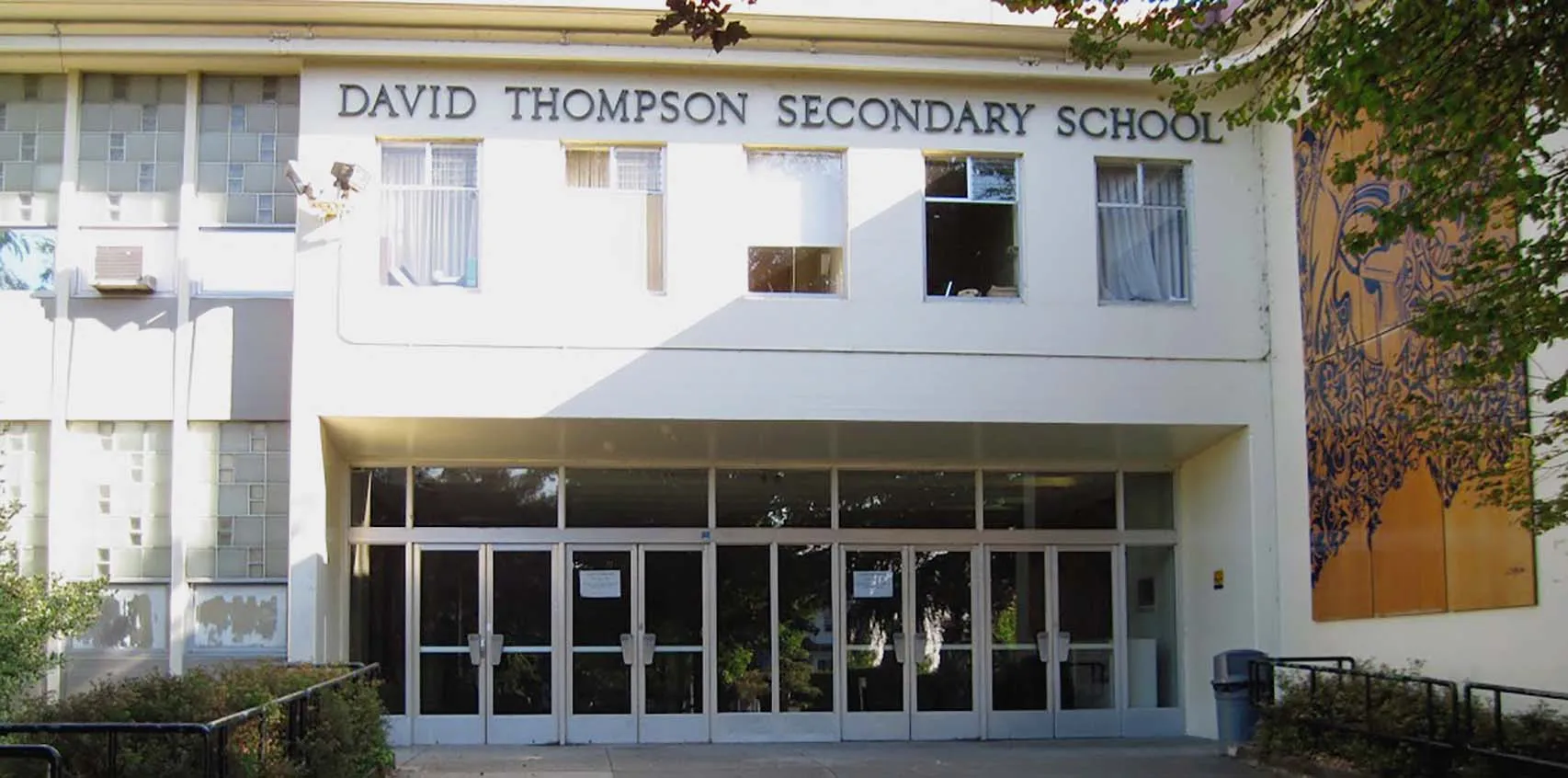 El edificio de la David Thompson Secondary School con una entrada de cristal y un árbol en primer plano.