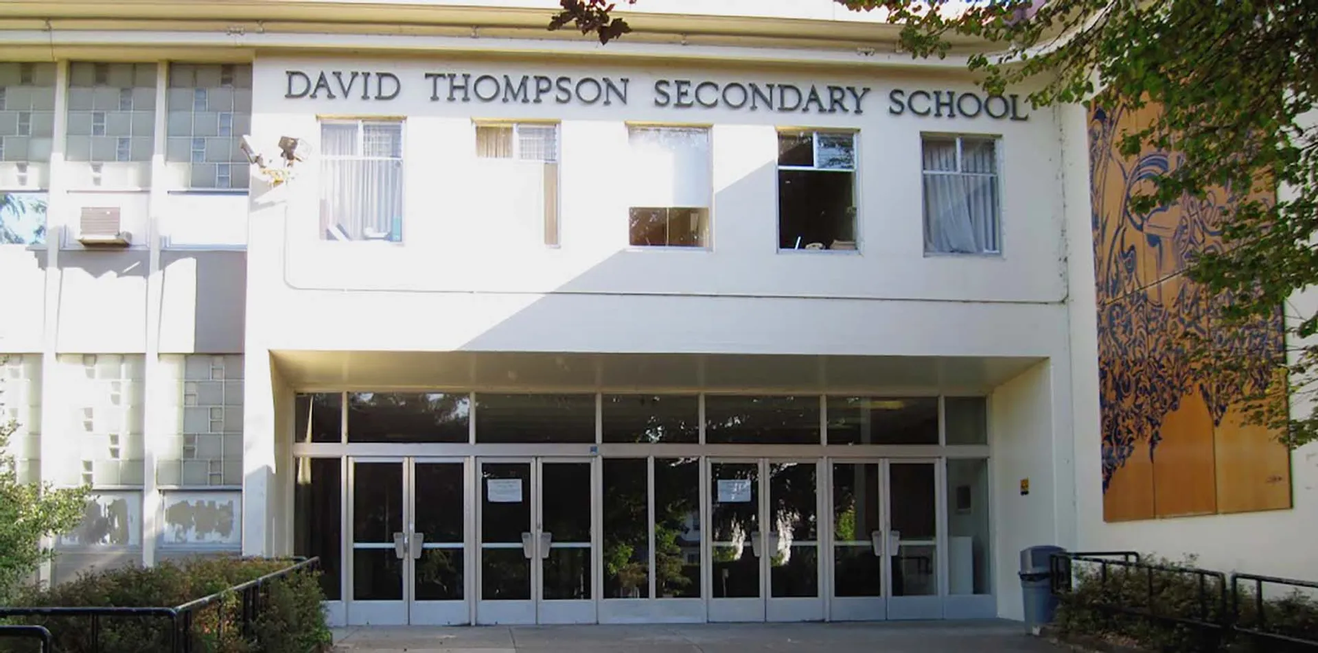 L'edificio della David Thompson Secondary School con un ingresso a vetri e un albero in primo piano.
