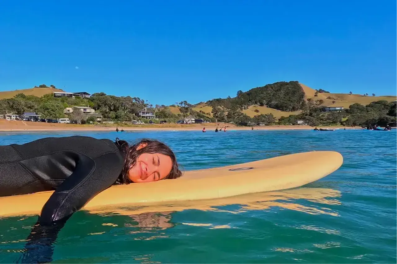 Studentessa in muta si rilassa sdraiata su una tavola da surf nell'acqua di una baia