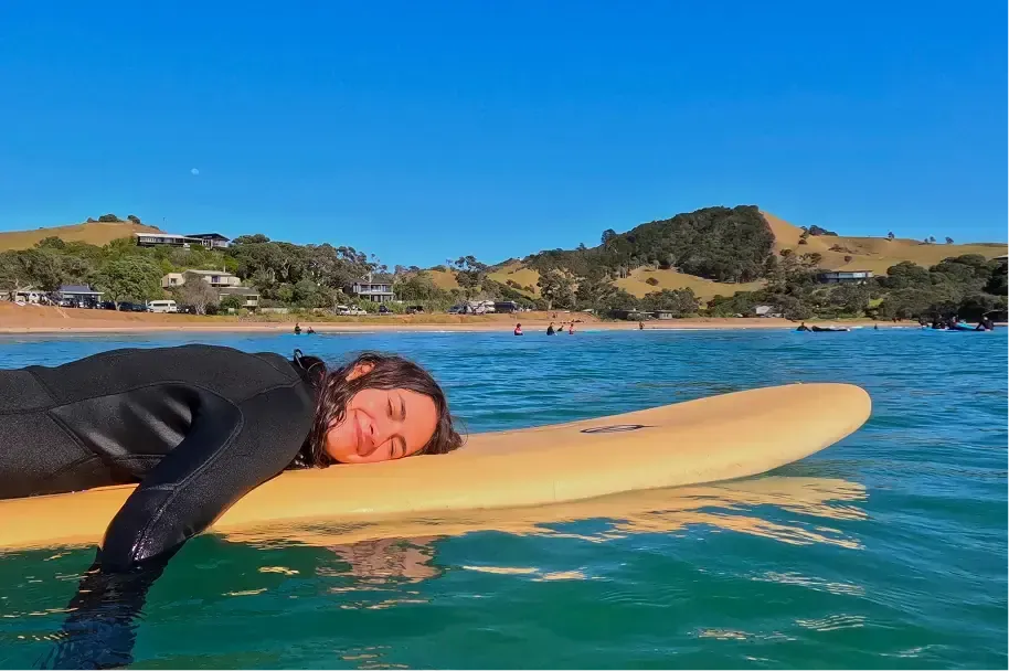 Studentessa in muta si rilassa sdraiata su una tavola da surf nell'acqua di una baia