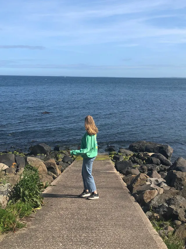 Chica de espaldas sobre un espigón de hormigón contemplando el mar