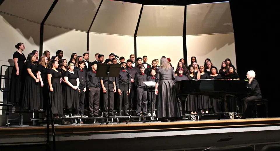 Studenti del St. Colmans College sono insieme su un palco in abito formale e cantano con un pianoforte in primo piano.