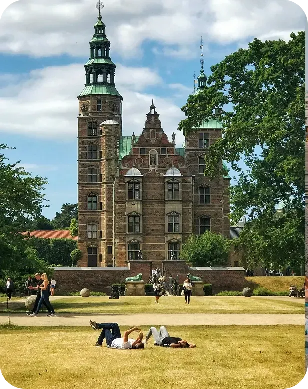 Persone rilassate sul prato di un parco davanti a un castello rinascimentale a Copenaghen