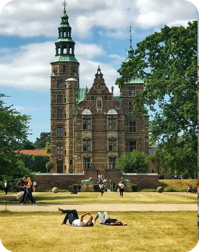 Persone rilassate sul prato di un parco davanti a un castello rinascimentale a Copenaghen