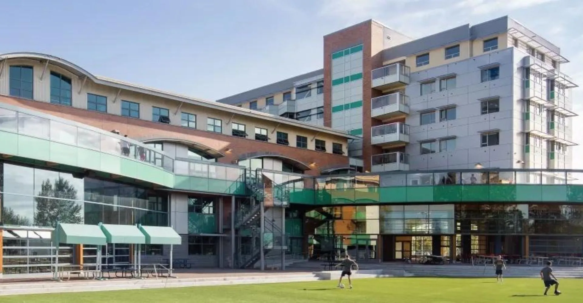 L'edificio scolastico moderno a più piani della Bodwell High School con archi e balconi circondato da un'area verde con persone.