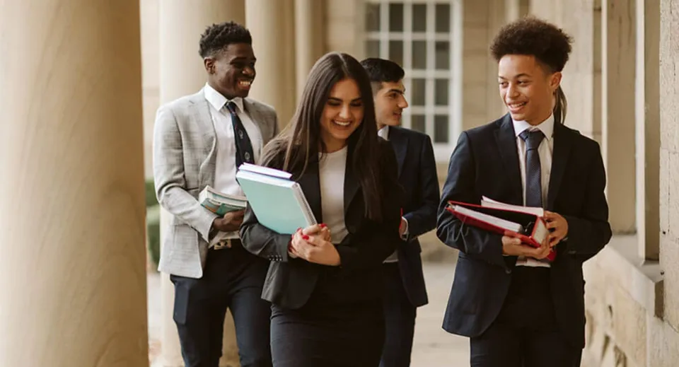 Un gruppo di studenti della Ackworth School cammina insieme davanti a un edificio con colonne portando libri e raccoglitori.